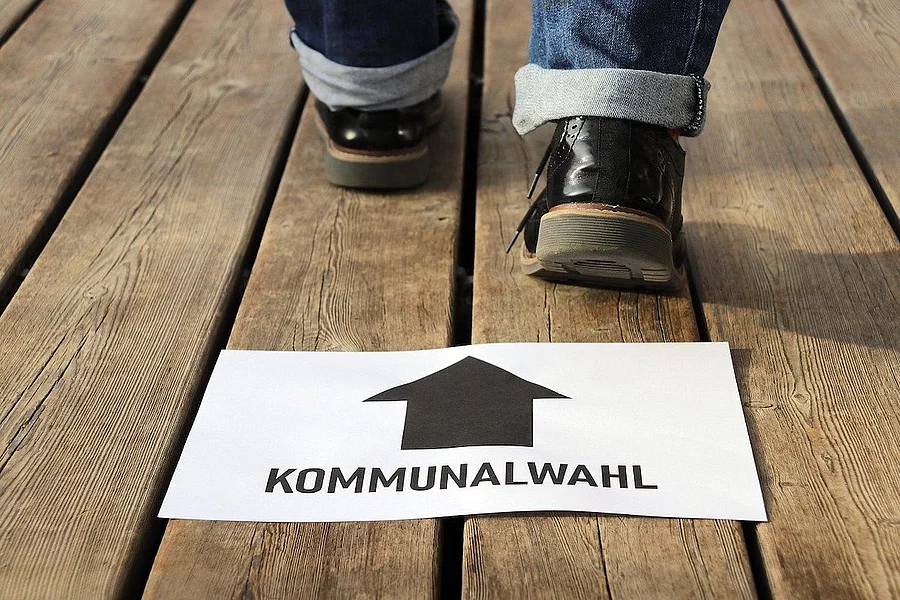 The picture shows a piece of paper with the words ‘LOCAL ELECTIONS’ and an upward-pointing arrow on a wooden floor, whilst feet wearing shoes can be seen in the background.