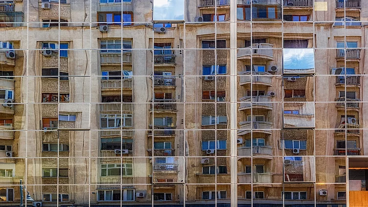 Fotografia prezintă fațada din sticlă reflectorizantă a unei clădiri moderne din București, în care se oglindesc clădiri rezidențiale mai vechi, în stil clasic.