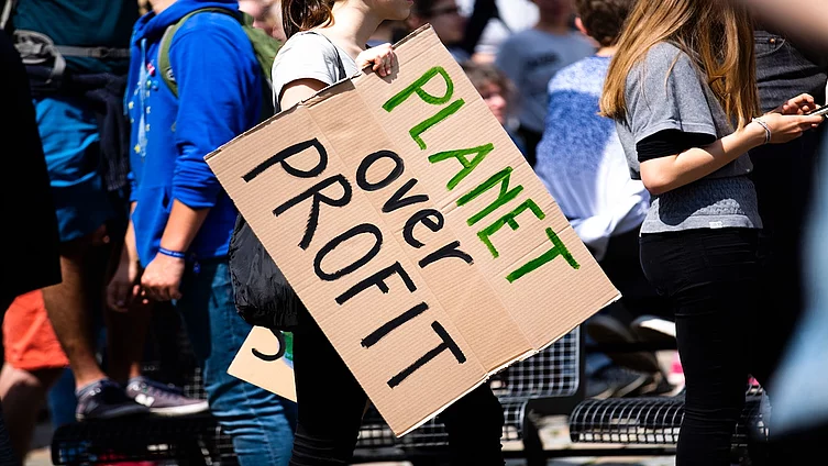 The picture shows a person holding a cardboard sign at a demonstration bearing the words ‘PLANET over PROFIT’. 