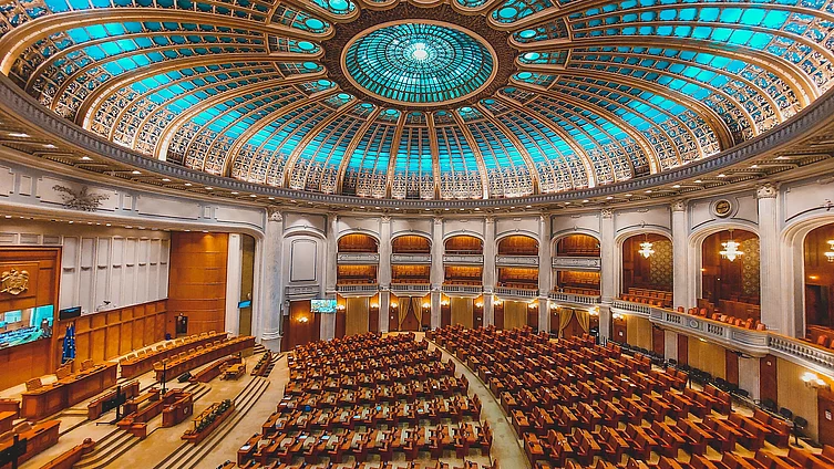 Fotografia prezintă interiorul sălii plenare a Camerei Deputaților din România, situată în Palatul Parlamentului din București, care se remarcă prin cupola sa impunătoare.