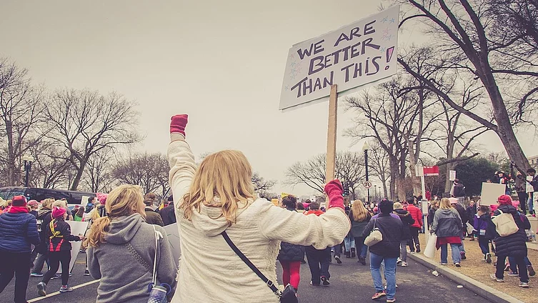 This photo shows a demonstration with people holding up a sign that reads “We are better than this!”