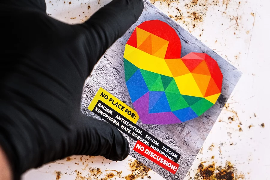 A hand wearing a black glove is holding a sticker featuring a colourful rainbow heart and the slogan ‘NO PLACE FOR: RACISM... NO DISCUSSION!’ to highlight the fight against discrimination.